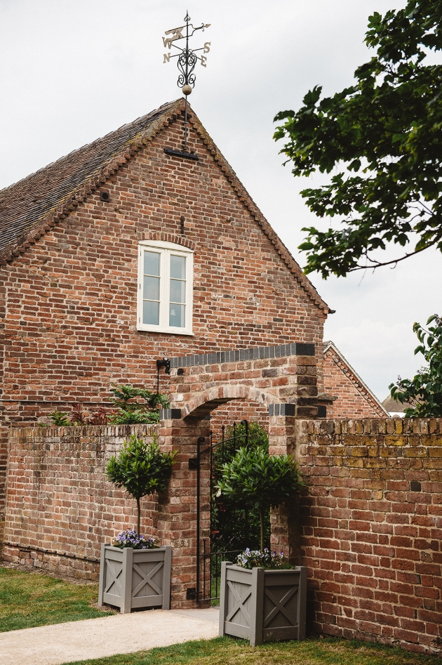 Alrewas Hayes, Staffordshire, view on the approach to the venue brick wall with flowers at  the entrance to the gardens