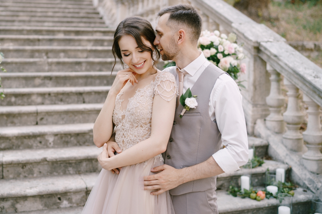 grooms with jacket off, beige waistcoats and trouses, hugging bride