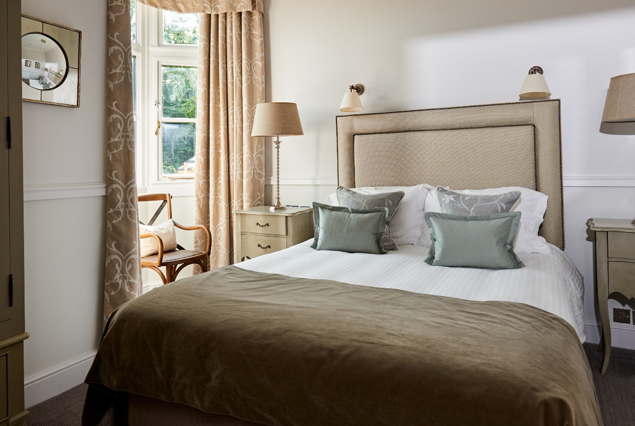 bed in a hotel room, beige walls beige flock curtains, bedside tables, chair in window