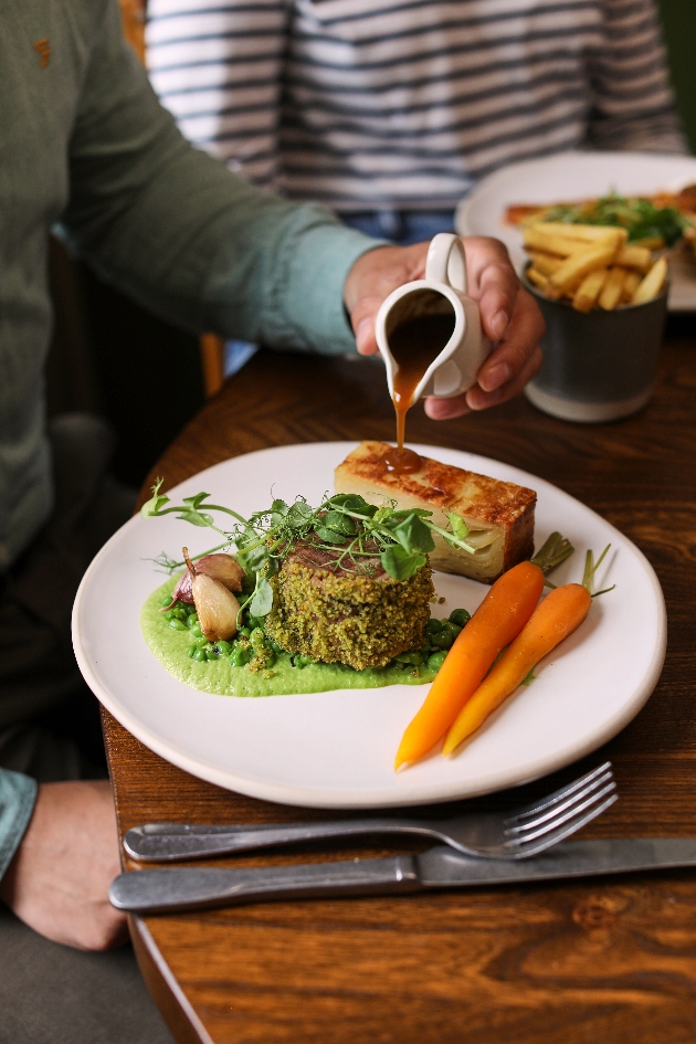 A person pouring gravy on their dinner