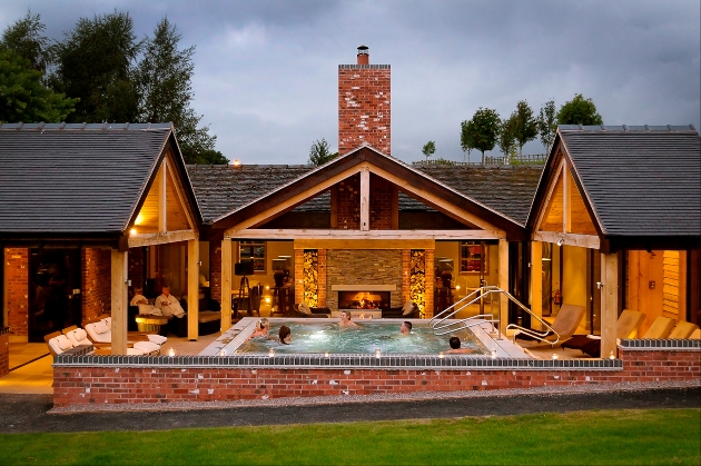 Five people in an outdoor swimming pool situated in front of a wood and brick building