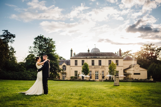 A bride and groom embracing in front of a large cream building