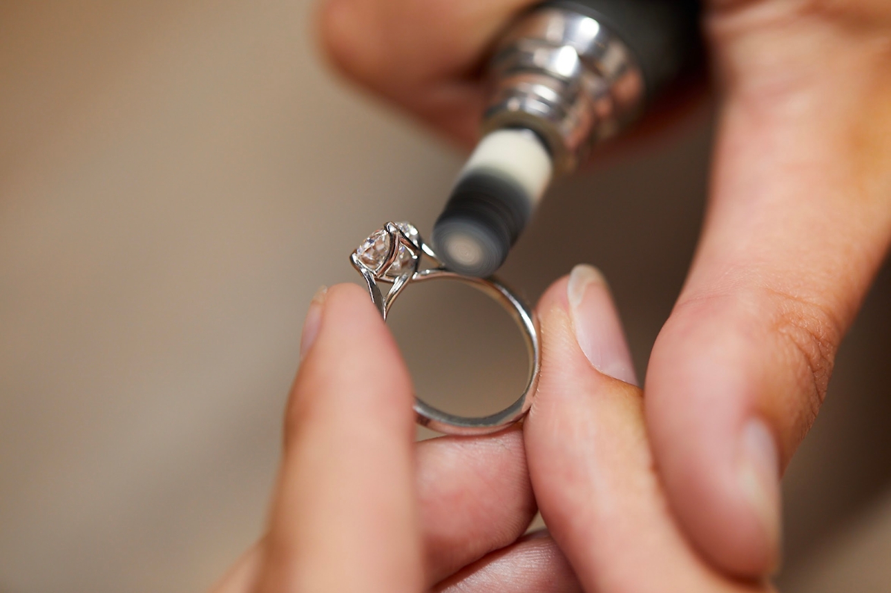 hands with tools working on making a diamond and silver ring