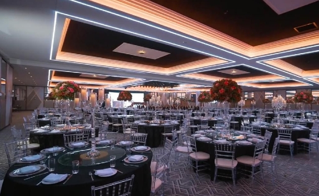 An indoor wedding breakfast set up with tall centrepieces and black table cloths