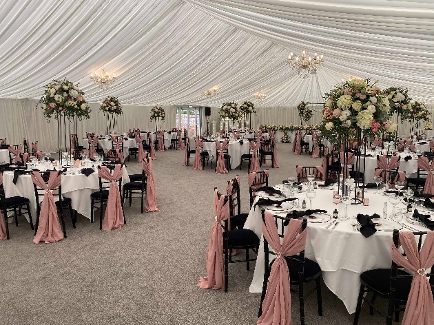 A wedding breakfast set up in a marquee with white table cloths and black chairs